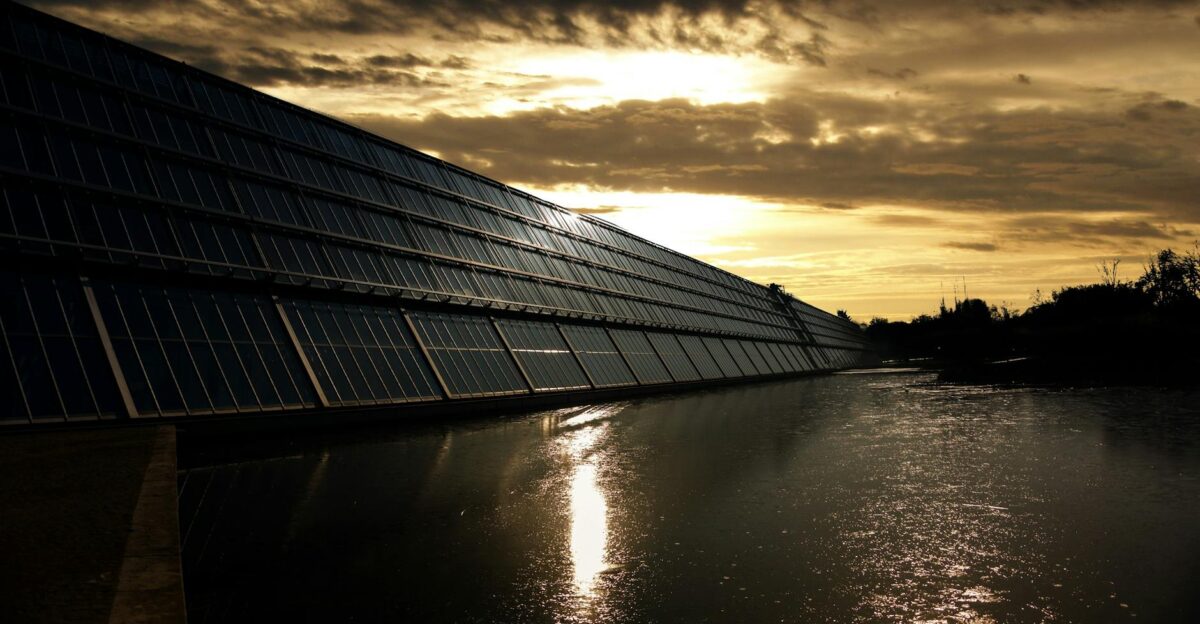 Silhouetted solar panels reflect sunset in tranquil waters showcasing renewable energy