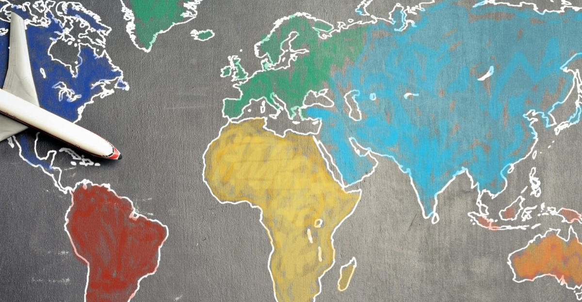 Top view of crop anonymous person holding toy airplane on colorful world map drawn on chalkboard