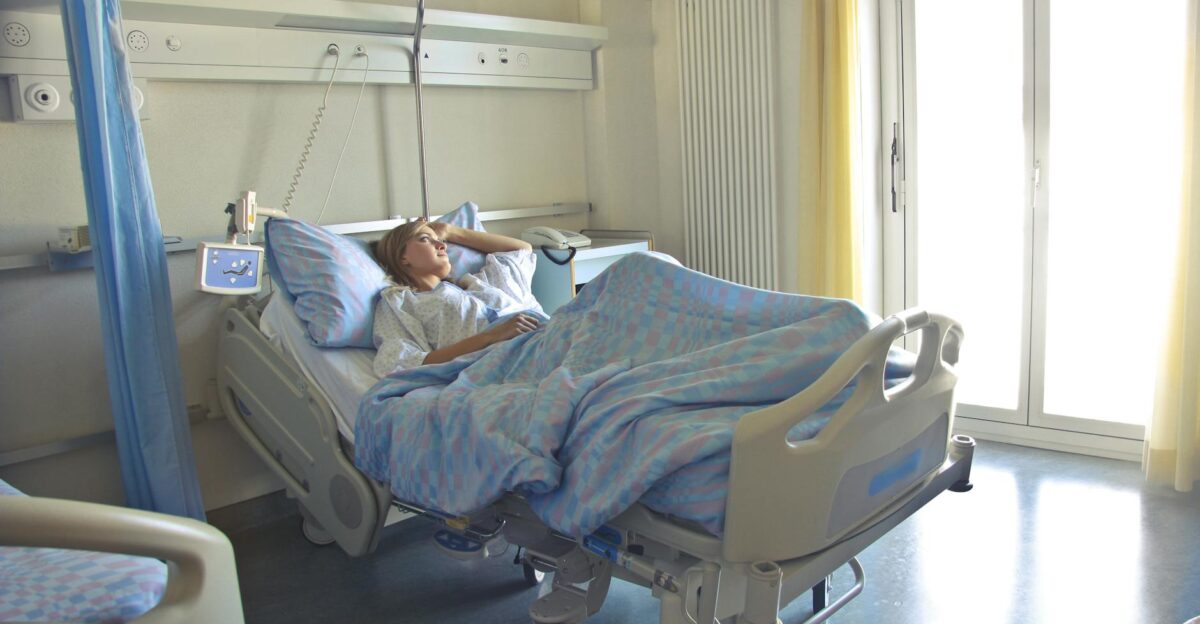 A woman lying in a hospital bed in a bright softly lit room appearing to rest or recover