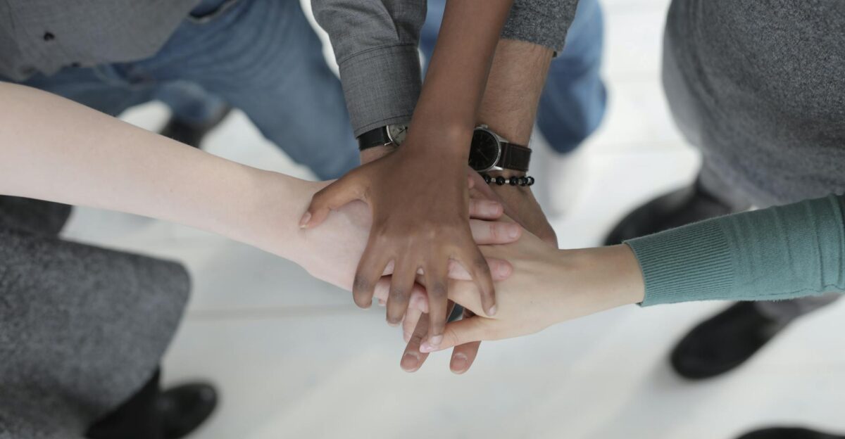Crop from above of faceless multiracial friends in casual clothes uniting hands after coming to agreement while standing on light grey ceramic floor