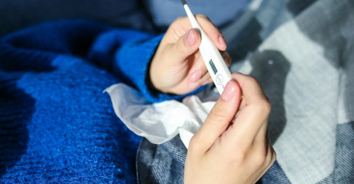 A woman checks a digital thermometer while lying indoors showing signs of illness