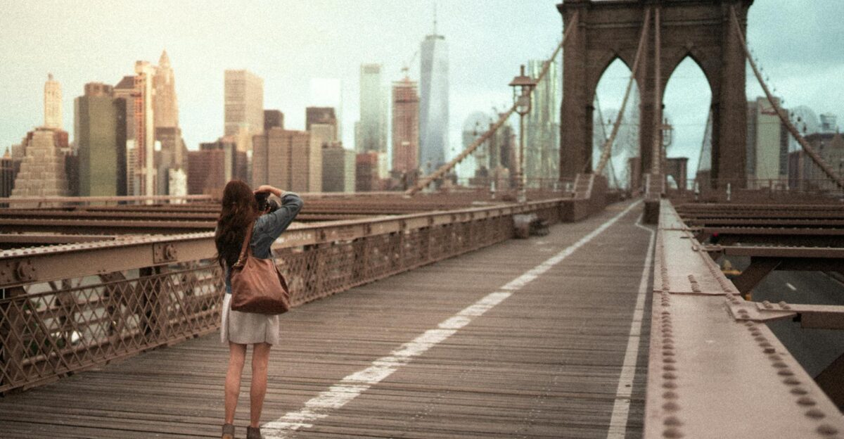 A woman captures the iconic Brooklyn Bridge with the NYC skyline in the background