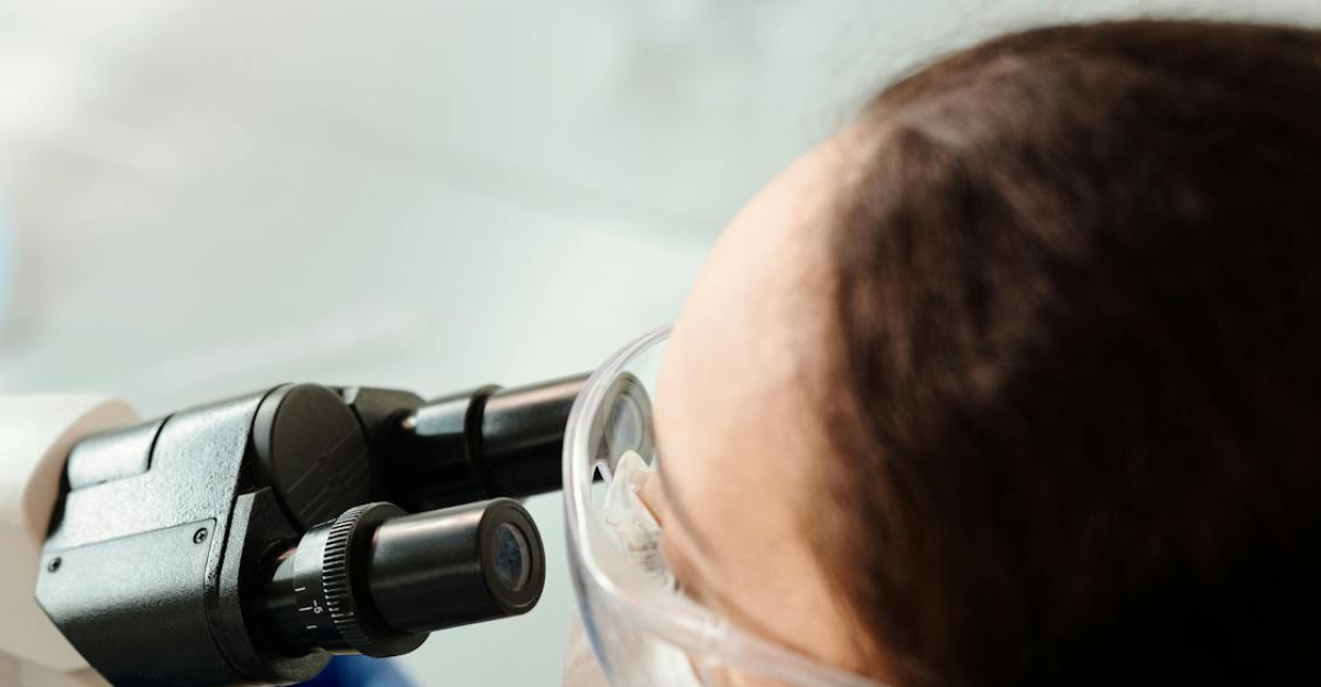 Scientist in protective gear examining samples with microscope in laboratory setting