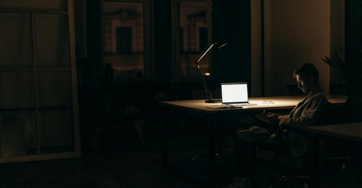 A man working late at night in a dimly lit office with a bright laptop screen