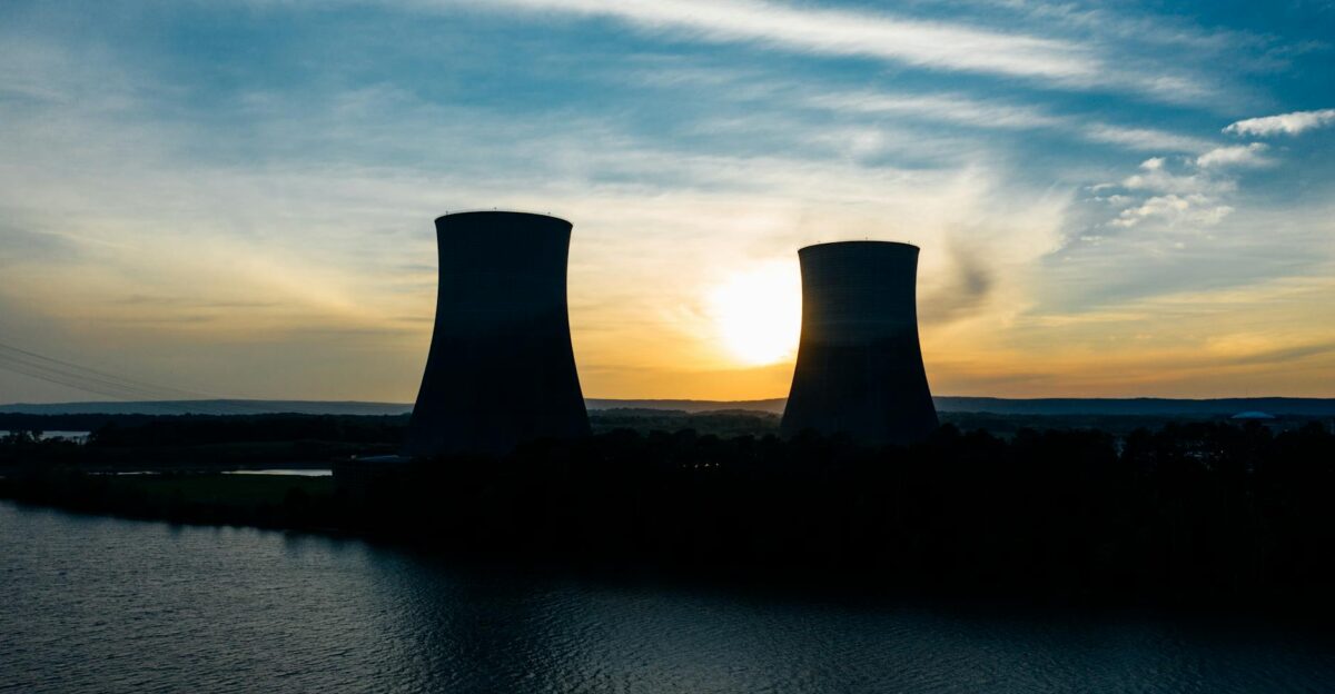 Identical cooling tower silhouettes on power plant near rippled river under colorful cloudy sky at sundown