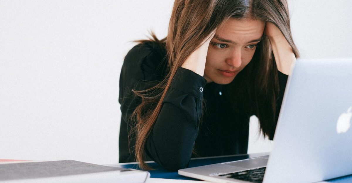 A stressed woman at a desk looking at a laptop with a worried expression