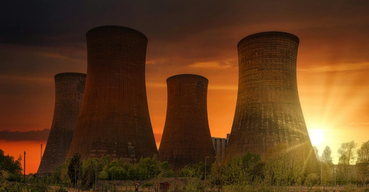 Exterior of huge cooling towers located in contemporary atomic power plant against bright setting sun under dramatic dark sky