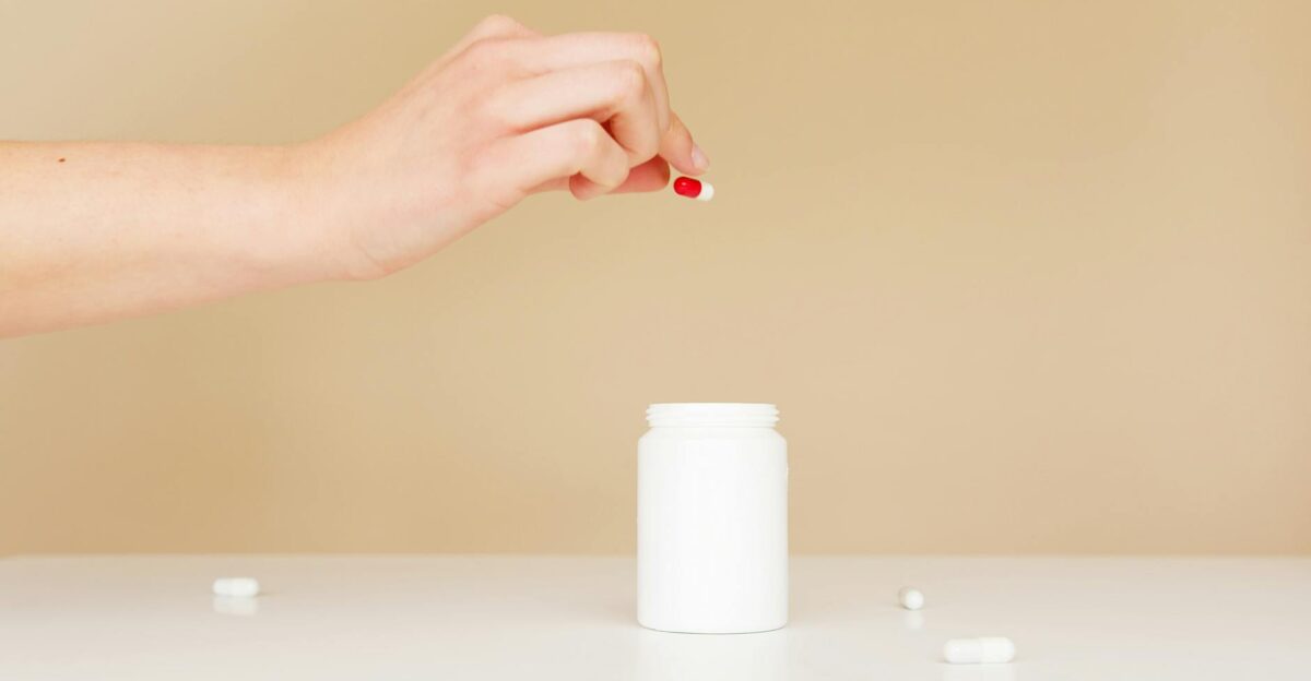 A close-up shot of a woman s hand holding a red and white capsule above a white bottle