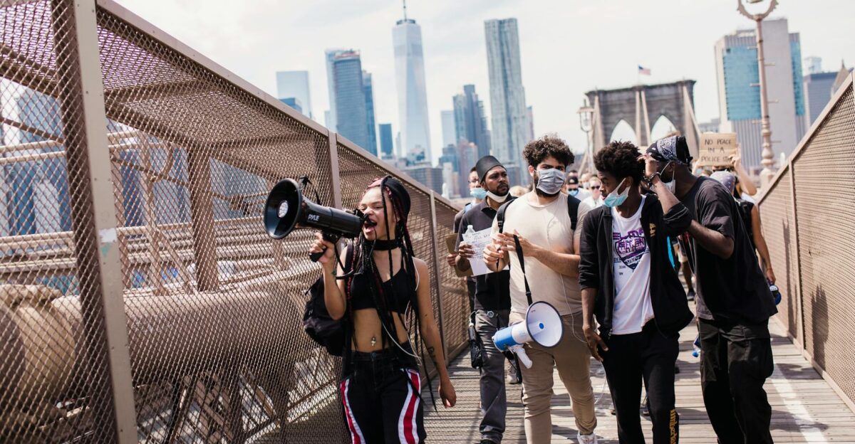 A diverse group of protesters march with megaphones on the Brooklyn Bridge advocating for justice and equality