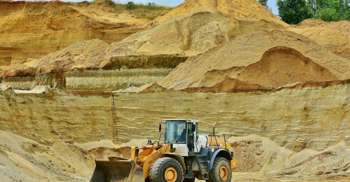 An excavator working in an open pit mine surrounded by sandy terrain and clear sky