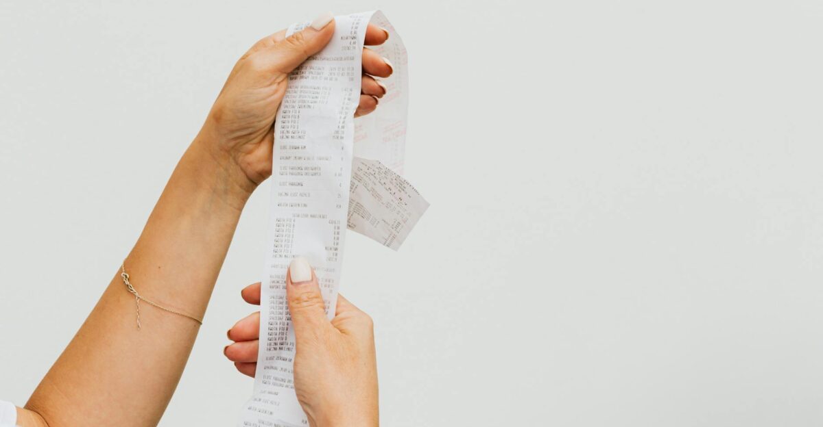 A detailed view of a person holding a long shopping receipt against a plain background