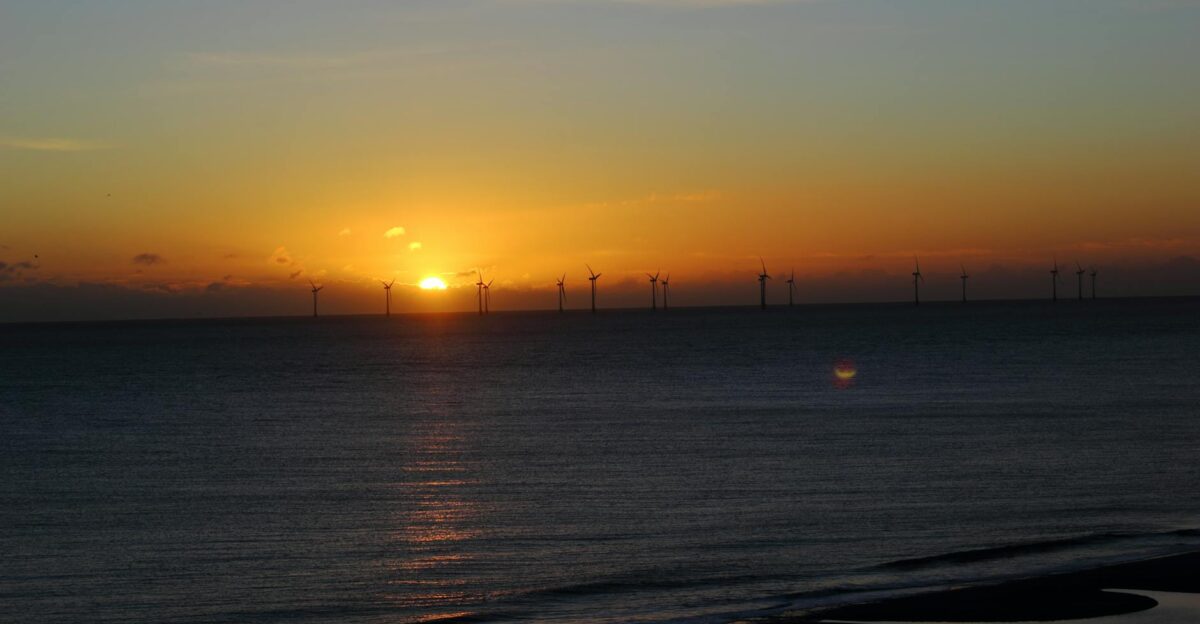 A scenic sunset view with wind turbines on the horizon reflecting in the sea