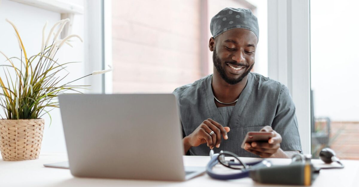 Smiling healthcare professional using phone in office with laptop and medical tools