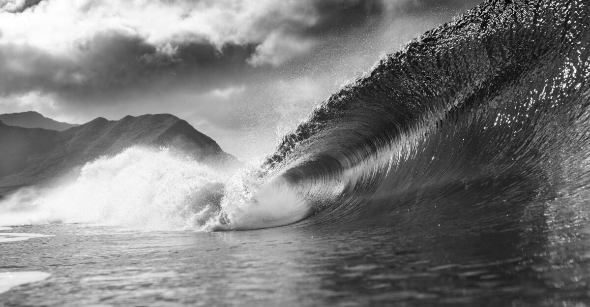 Black and white of foamy wave falling into ocean with splashes against cloudy sky in summer day in nature outside