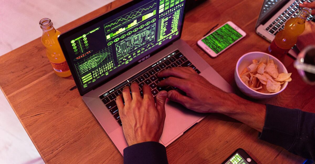 Hands typing on a laptop with coding phone on desk symbolizing cybersecurity