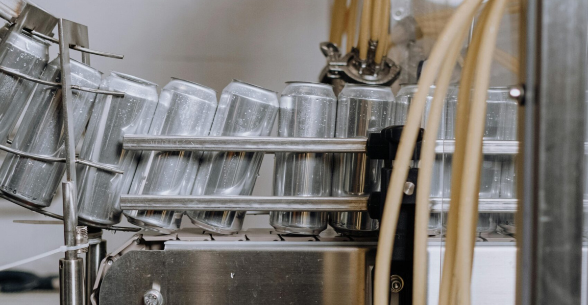 Vertical shot of an automated canning machine in a beverage factory showing aluminum cans in production.
