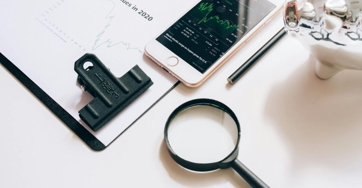 Flat lay of financial tools including a smartphone with stock data magnifying glass and chart