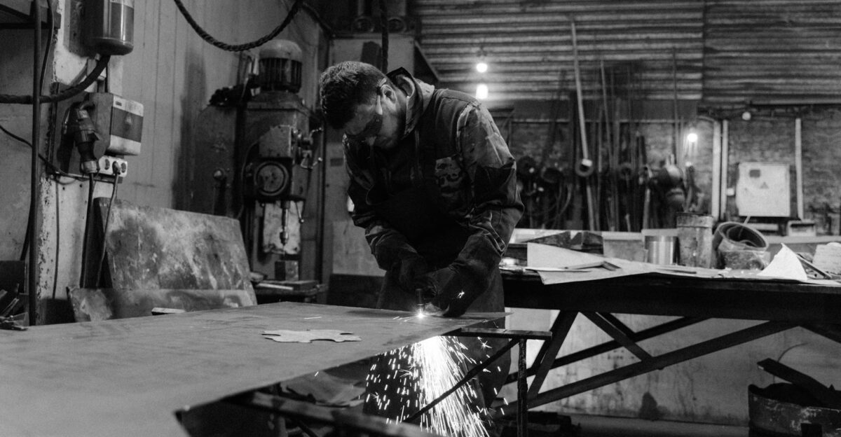 A skilled worker welding metal in an industrial factory setting in black and white