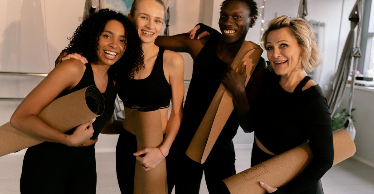 A cheerful group of diverse adults holding yoga mats in an indoor studio setting
