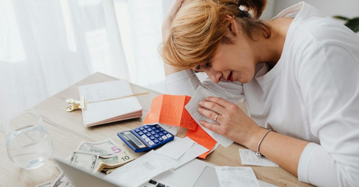 A woman overwhelmed with finances surrounded by bills calculator and cash at home