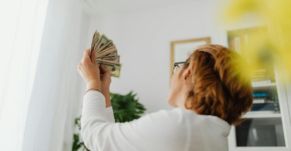 A person raises a fan of dollar bills indoors indicating wealth or success