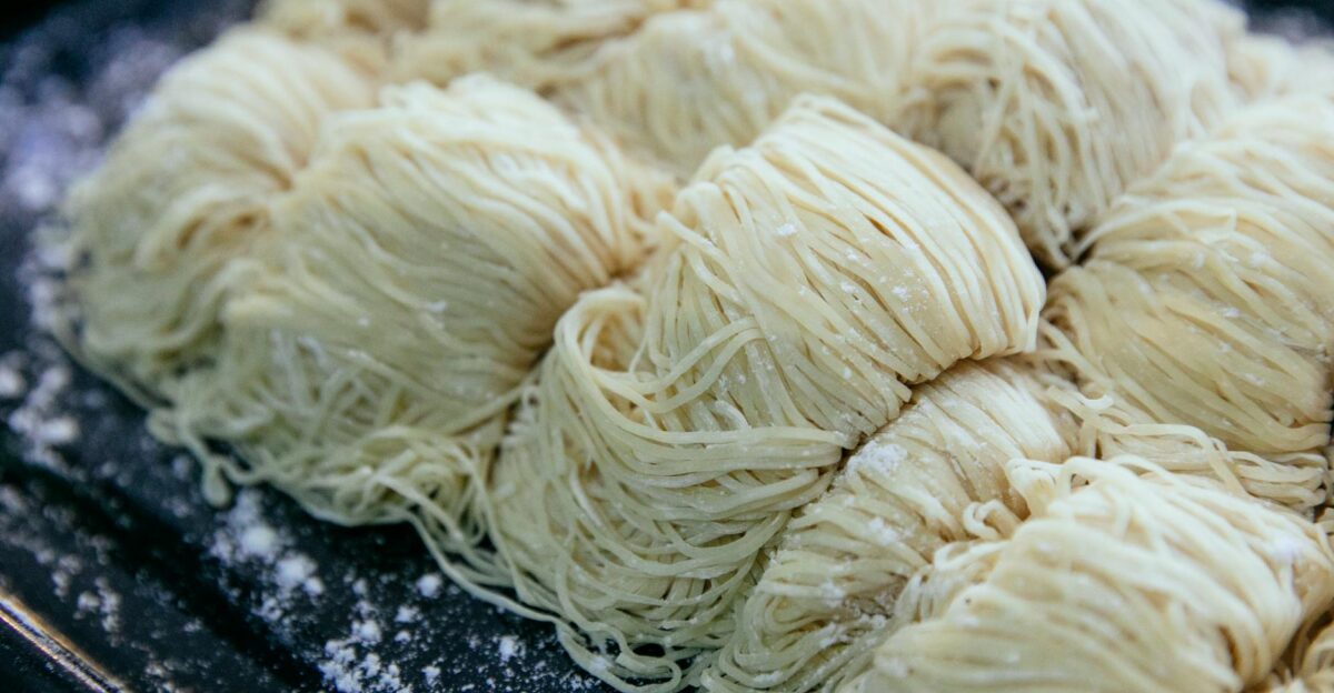 Homemade egg noodles collected in rolls and sprinkled with flour on black baking sheet