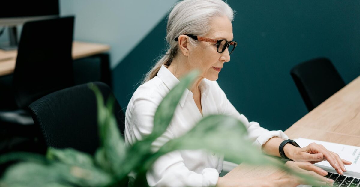 Confident senior woman with glasses working on a laptop in a modern office setting