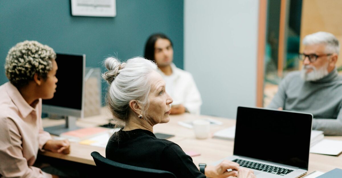 A multicultural team engaged in a meeting around a conference table with laptops