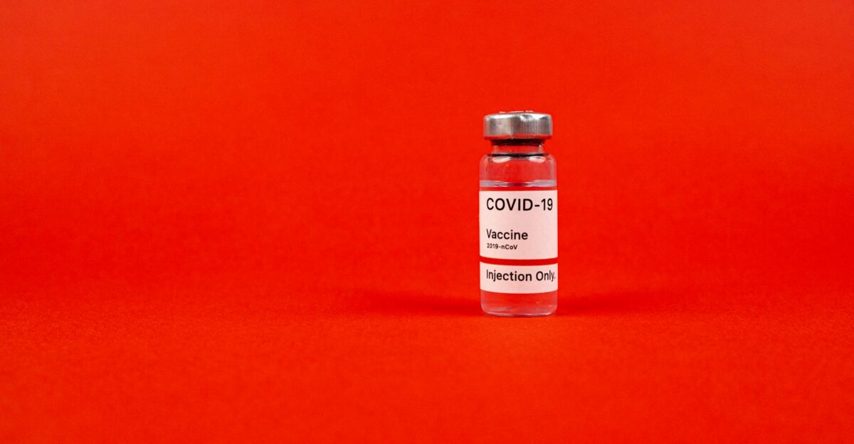 Glass vial of COVID-19 vaccine on a vibrant red backdrop emphasizing protection