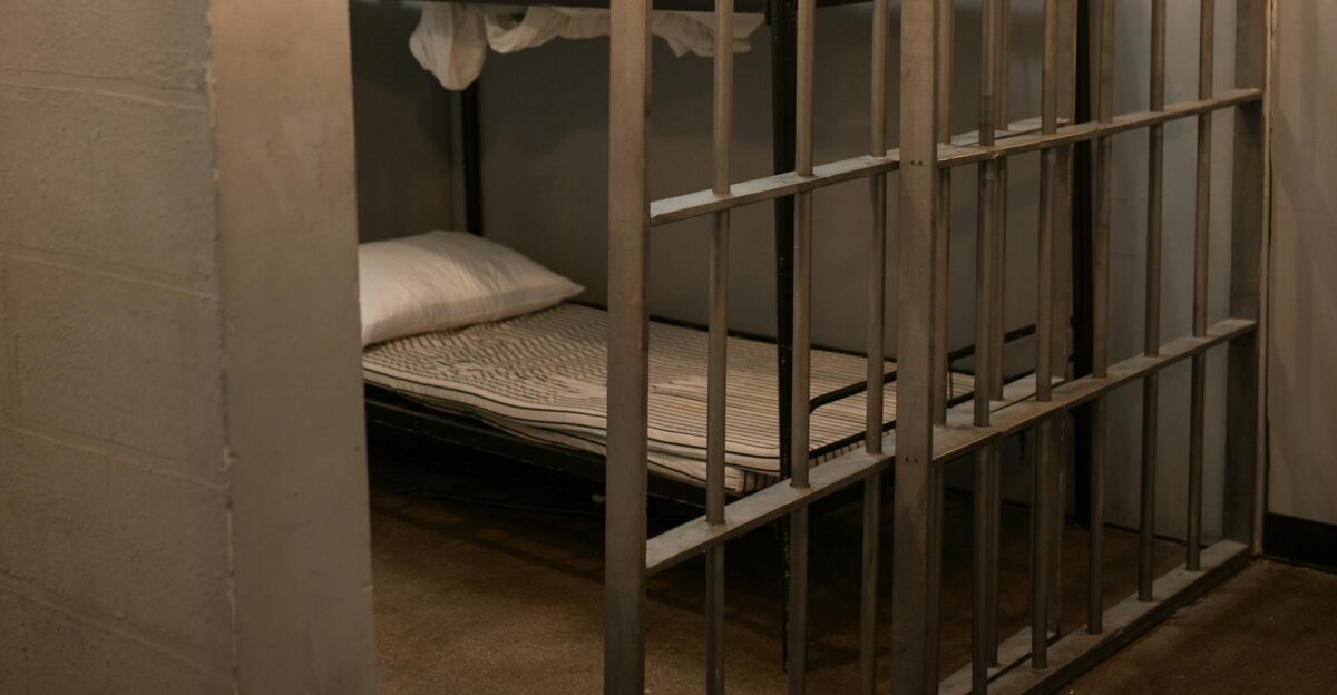 A prison cell featuring a metal bunk bed and striped sheets