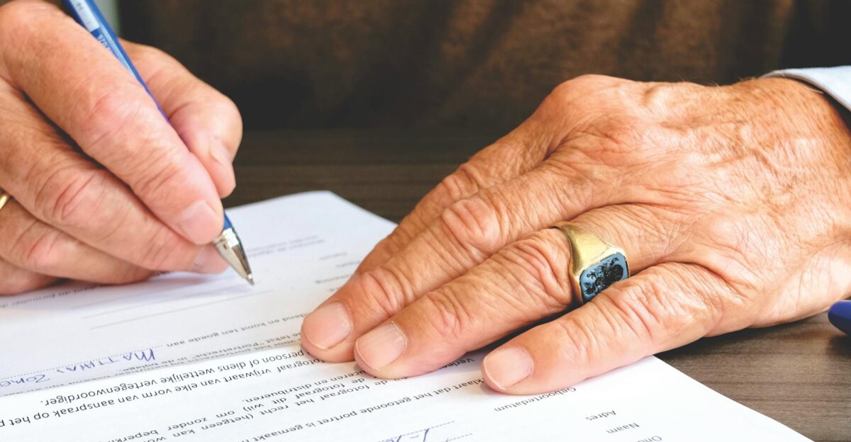 Close-up of a senior adult signing a legal document with a focus on hand and gold ring