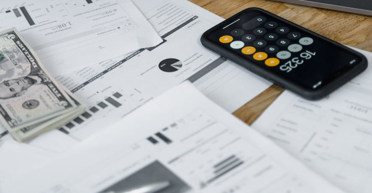 Hands counting money at a workspace with a laptop calculator and financial documents