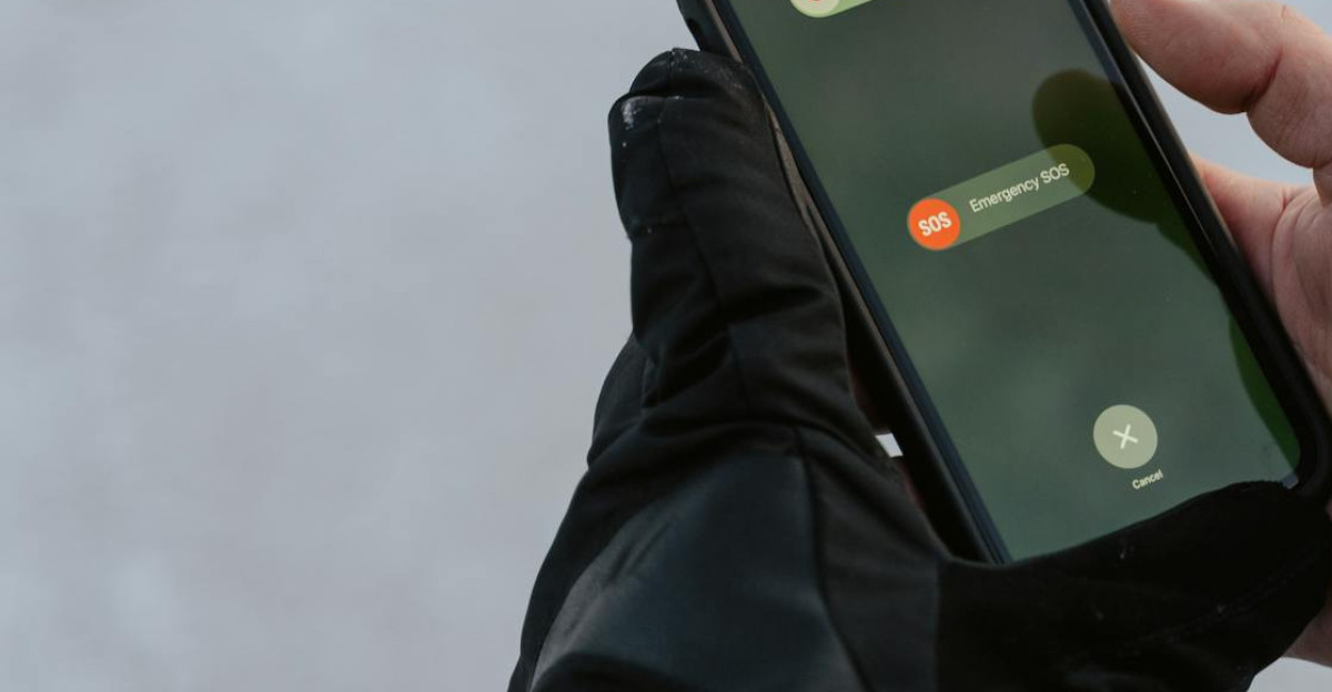 Gloved hands holding a smartphone displaying an emergency SOS screen