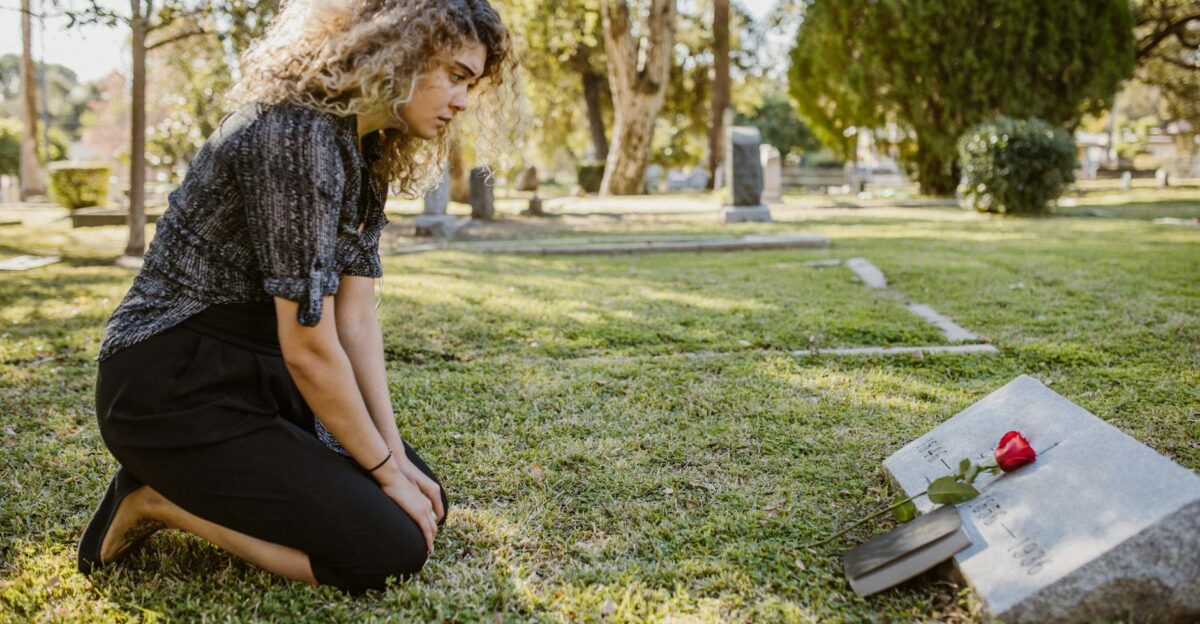 A woman kneeling by a grave in a sunlit cemetery expressing grief and remembrance