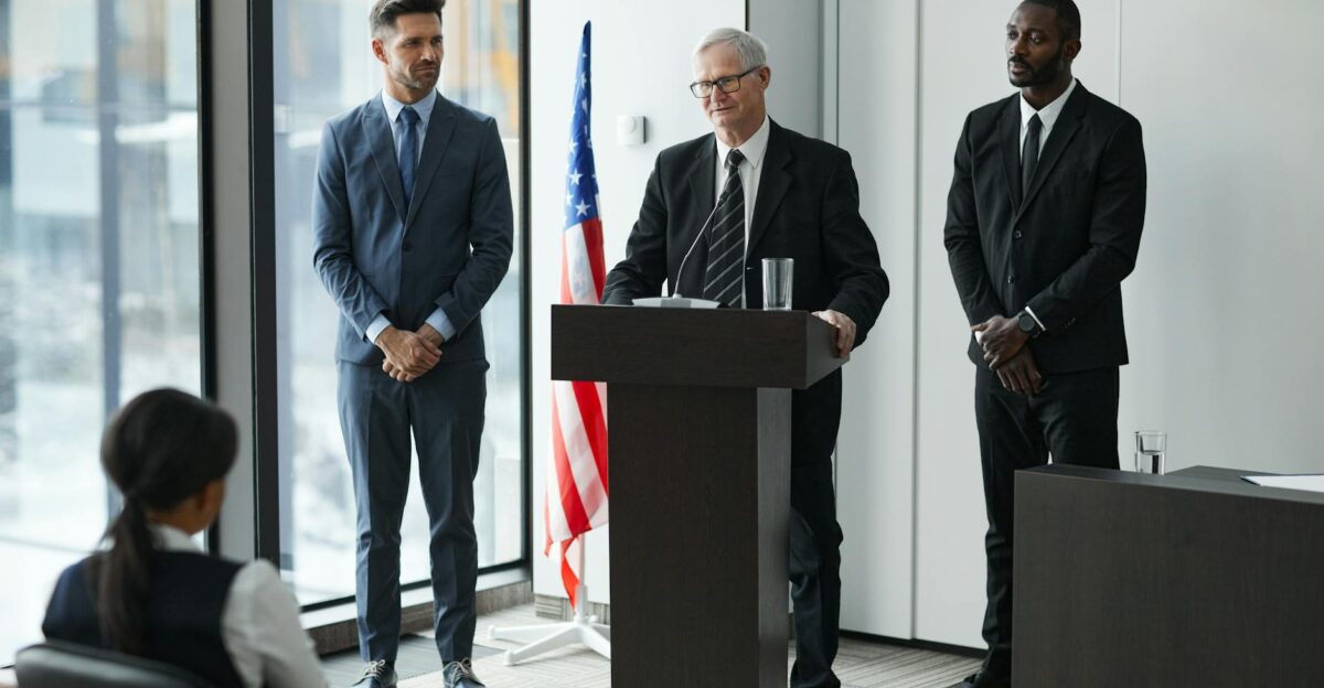 Officials delivering a political speech in a modern conference room with an American flag