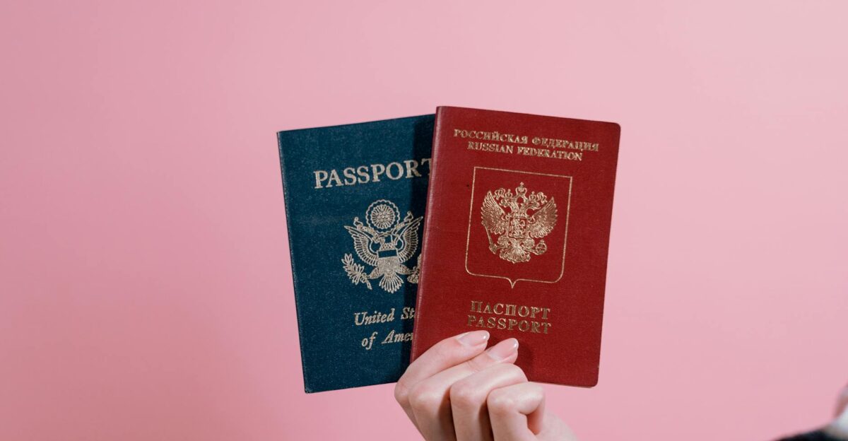 Close-up of a hand holding American and Russian passports on a pink background