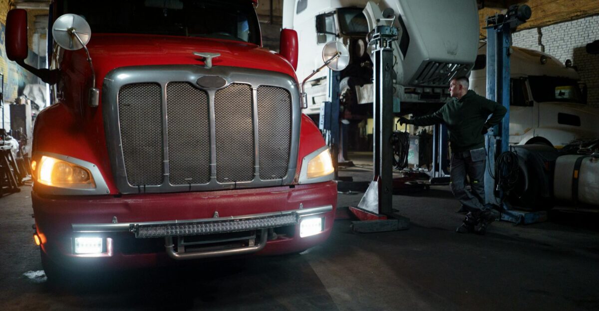 Red truck in a garage with mechanic and elevated vehicles undergoing maintenance