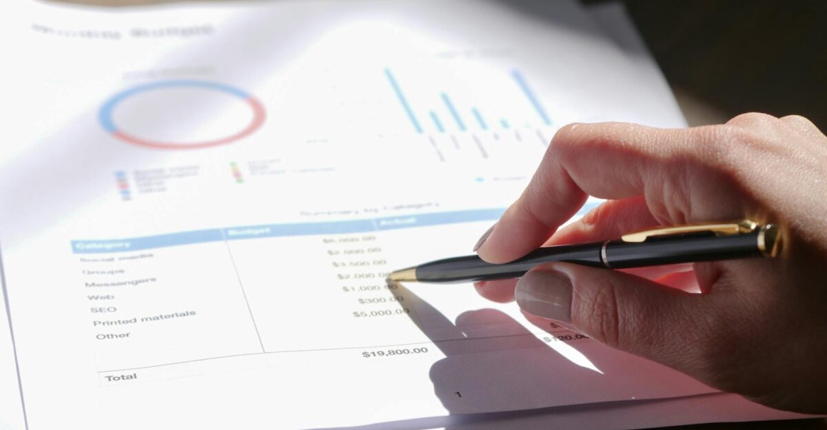 Hand holding pen analyzing budget with charts and graph paper