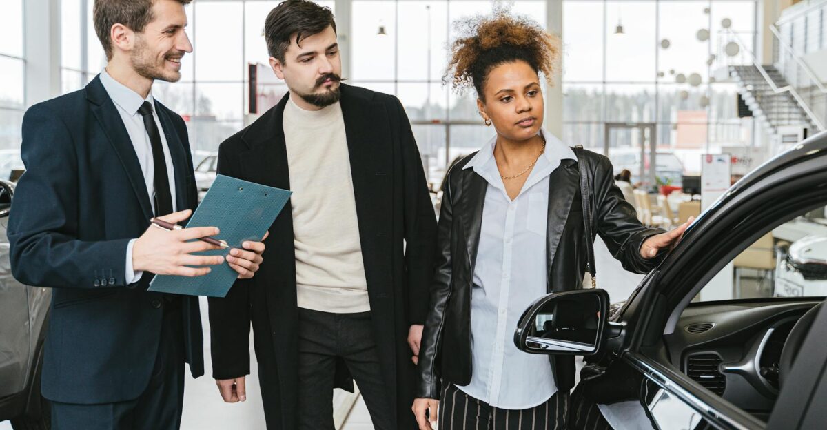 An interracial couple consults with a salesman at a car dealership exploring vehicle options