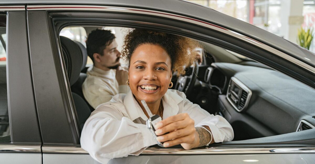 Joyful couple in their new car holding keys in a dealership showroom smiling warmly