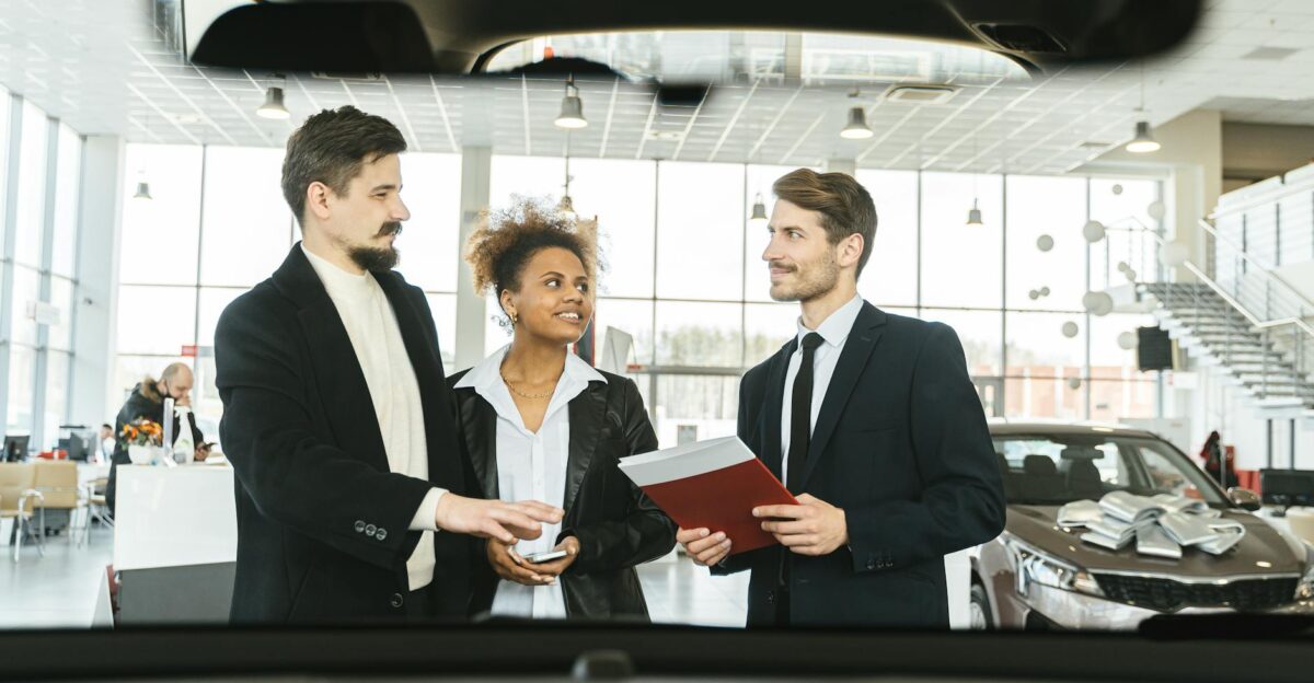 A diverse group of three people discussing car buying options indoors at a dealership