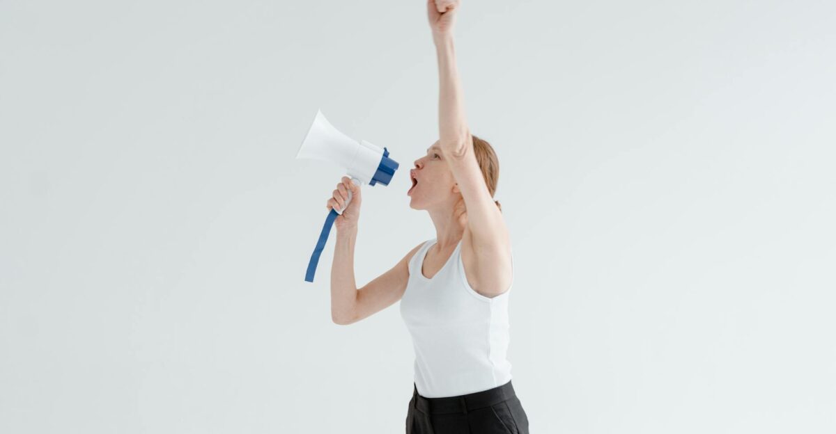 A confident woman raises her arm while shouting into a megaphone symbolizing leadership and empowerment