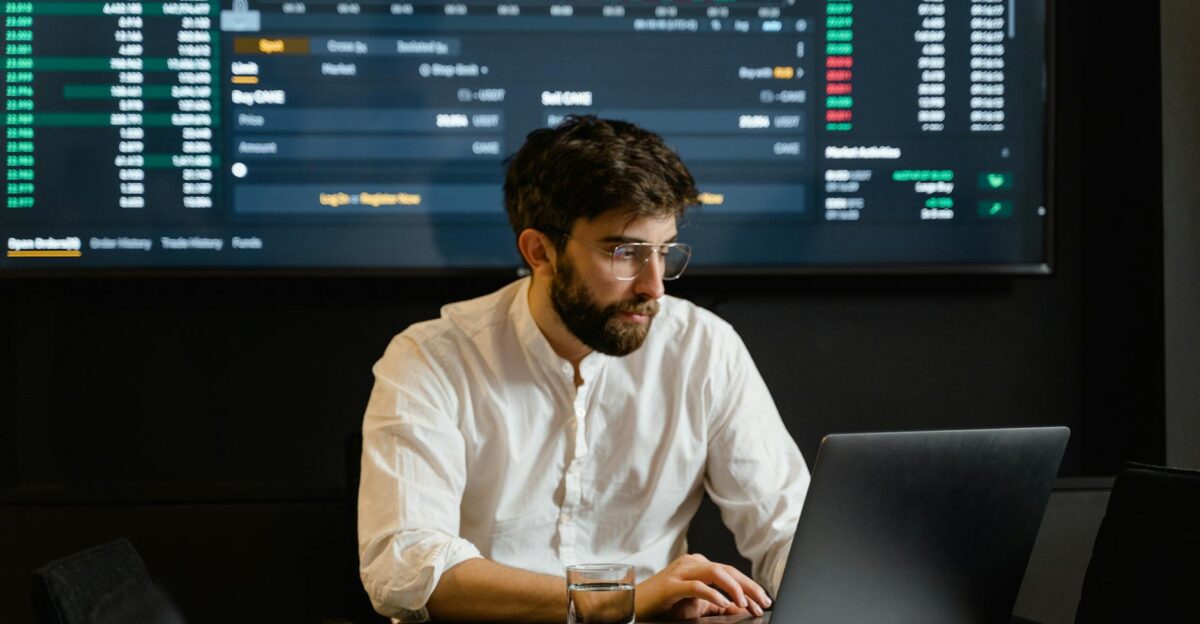 Professional analyzing stock market trends using laptop and digital display in modern office