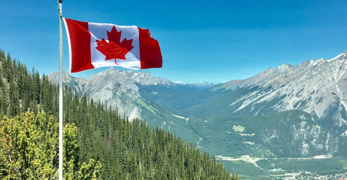Canadian flag waving atop a scenic mountain view with blue skies and lush greenery