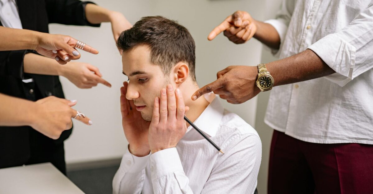 A stressed man at the office surrounded by pointing fingers representing workplace bullying and stress