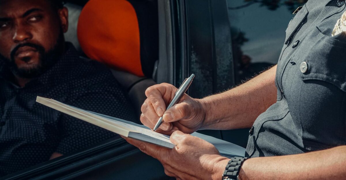 A police officer writes a ticket as the driver looks on from inside the car