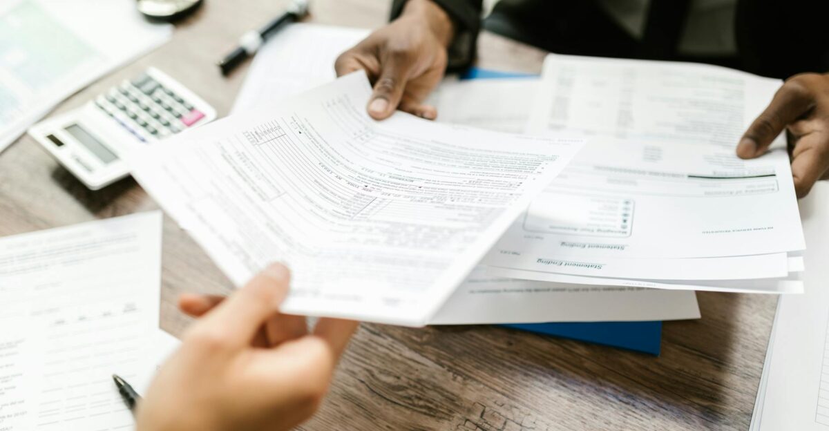 Two professionals exchanging documents in an office setting focusing on paperwork and data analysis
