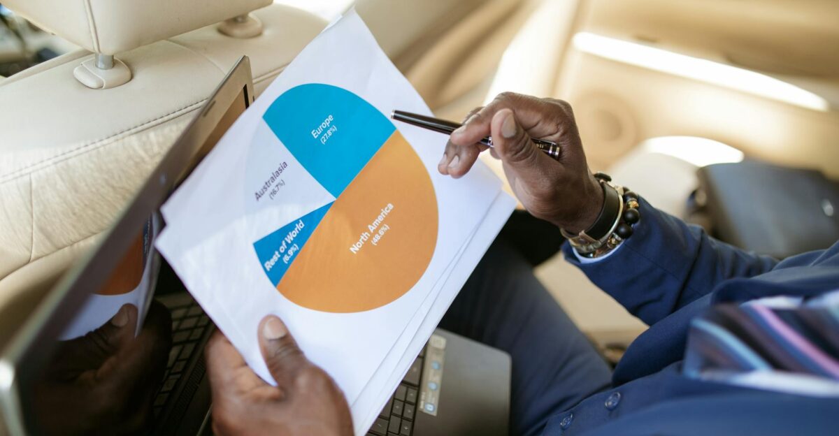 Businessperson in car reviewing a pie chart report on laptop