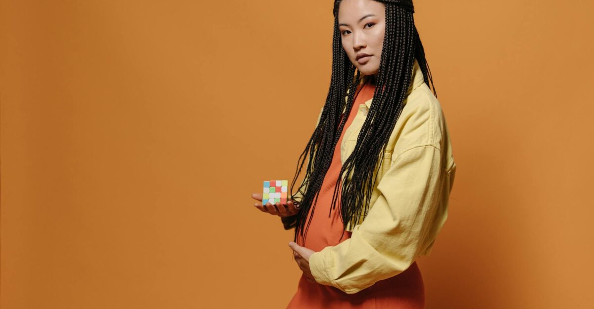 Portrait of a fashionable woman with braids holding a Rubik s Cube against an orange backdrop