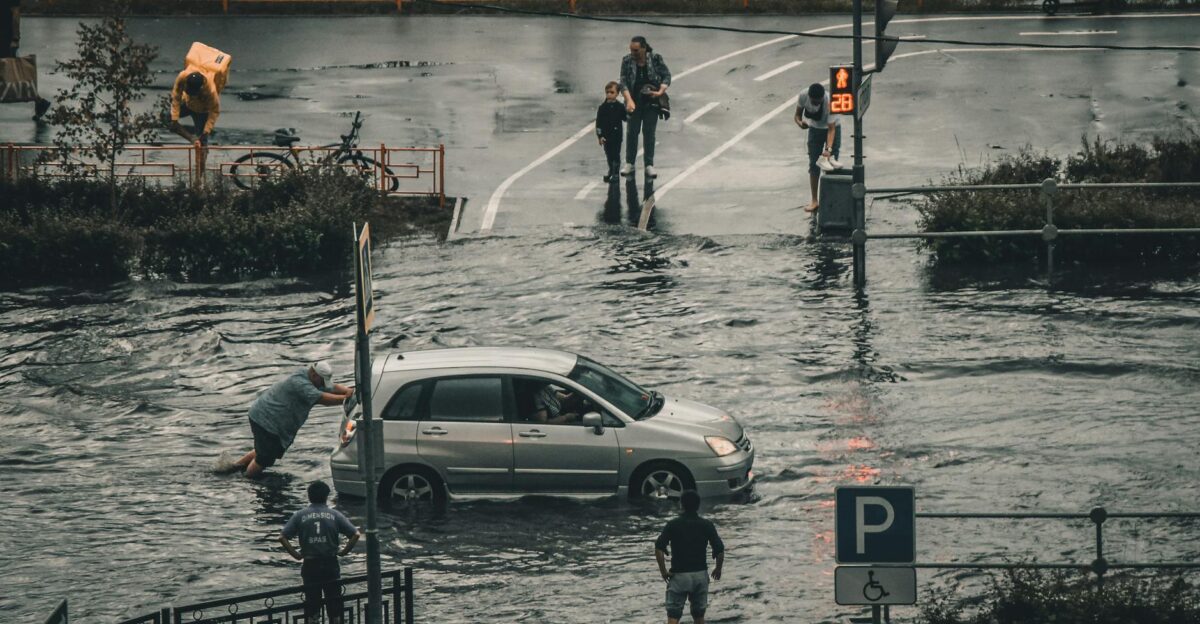 A flooded city street with a car being pushed and pedestrians navigating the water